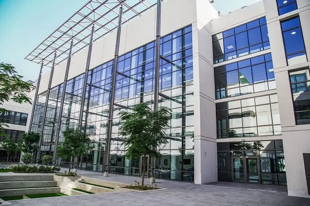The glass front of the school campus building behind young trees