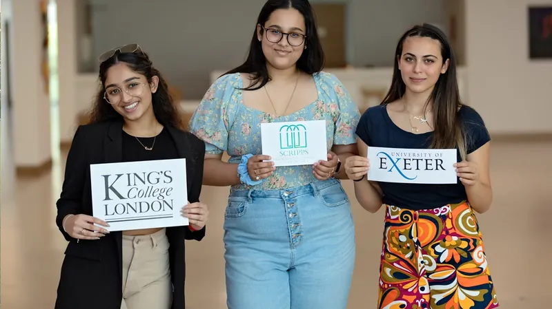Three leavers hold signs for King's College London and the University of Exeter