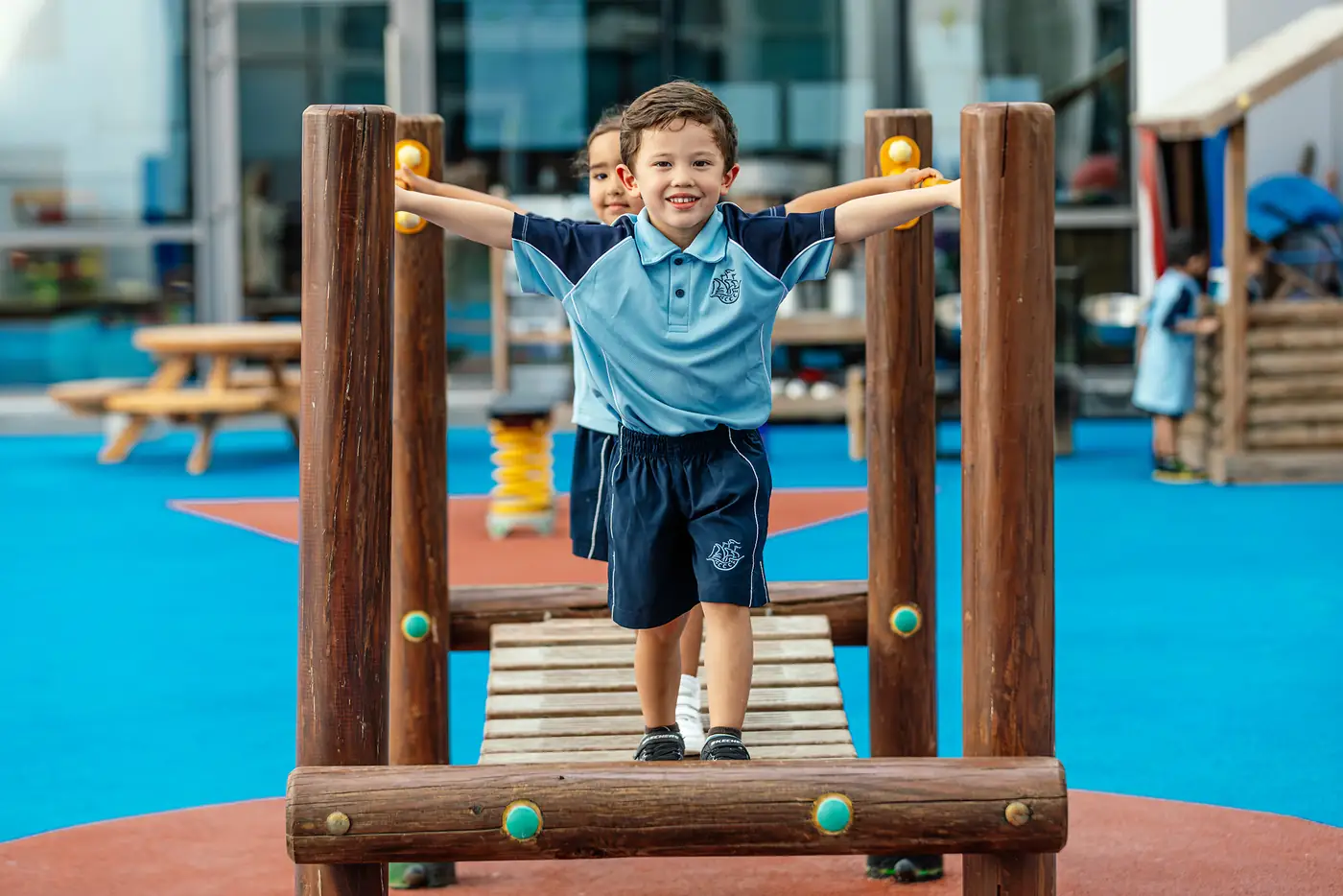 A young child balances along a wooden climbing frame with both arms raised