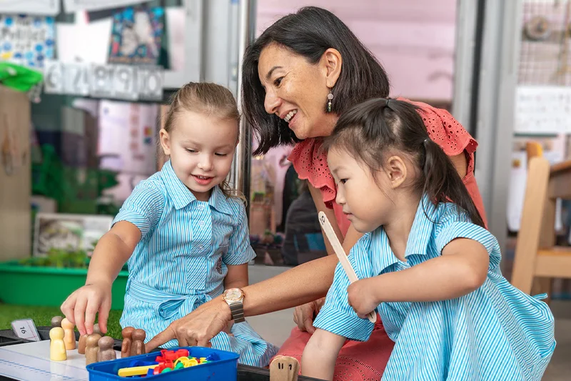 A teacher plays with two Early Years children at a table of coloured blocks